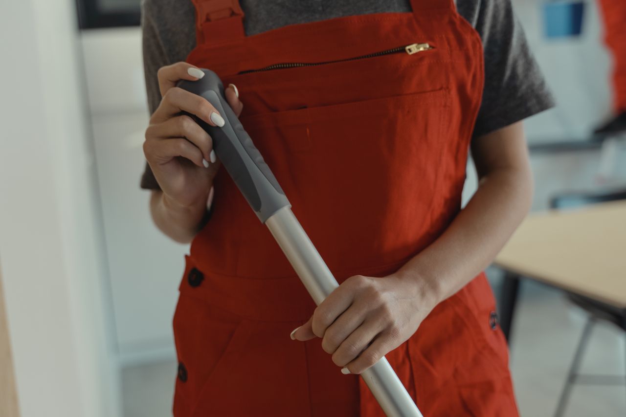 services-01 A woman in a red apron holding a mop handle, performing cleaning indoors.